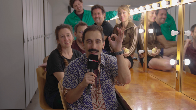 L'actor Albert Roig al camerino de figuració del Liceu amb un micròfon entrevistant a cinc figurants de l'òpera Lady Macbeth de Mtsenk, asseguts al seu voltant.